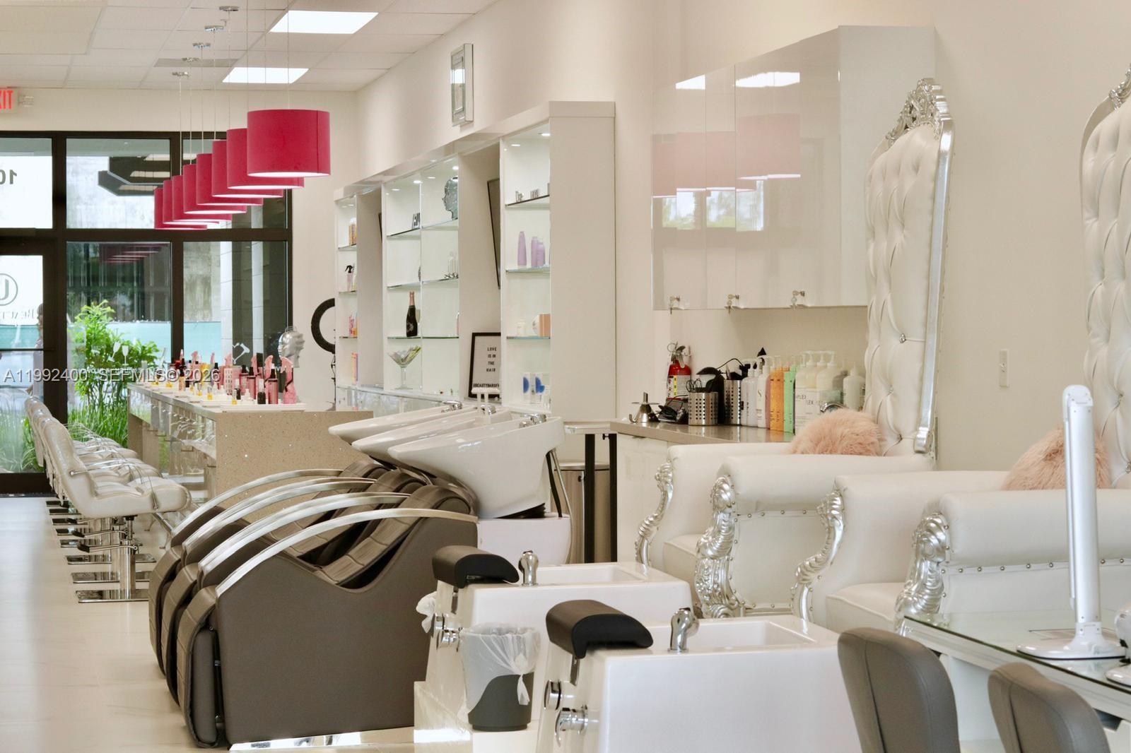 A modern salon interior features shampoo stations, white throne-style chairs, and bright pink pendant lighting — 12700 SW 128th St, Miami FL 33186, MIAMI, FL