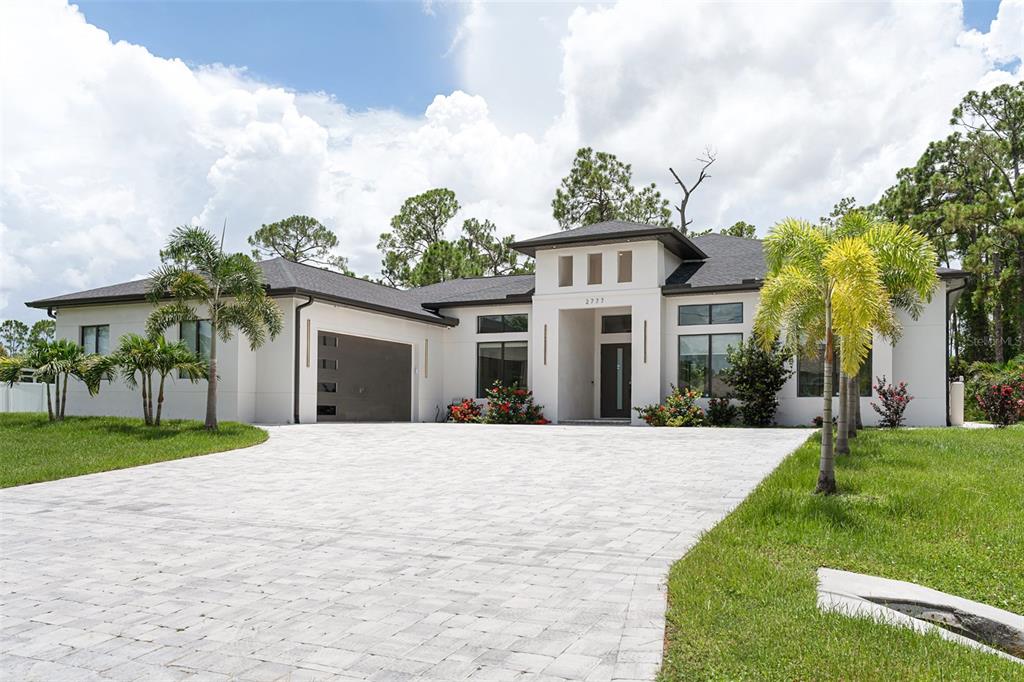 A modern white single-story house features a paved driveway, dark roof, and palm trees — 2777 LUCAYA AVENUE, NORTH PORT, FL