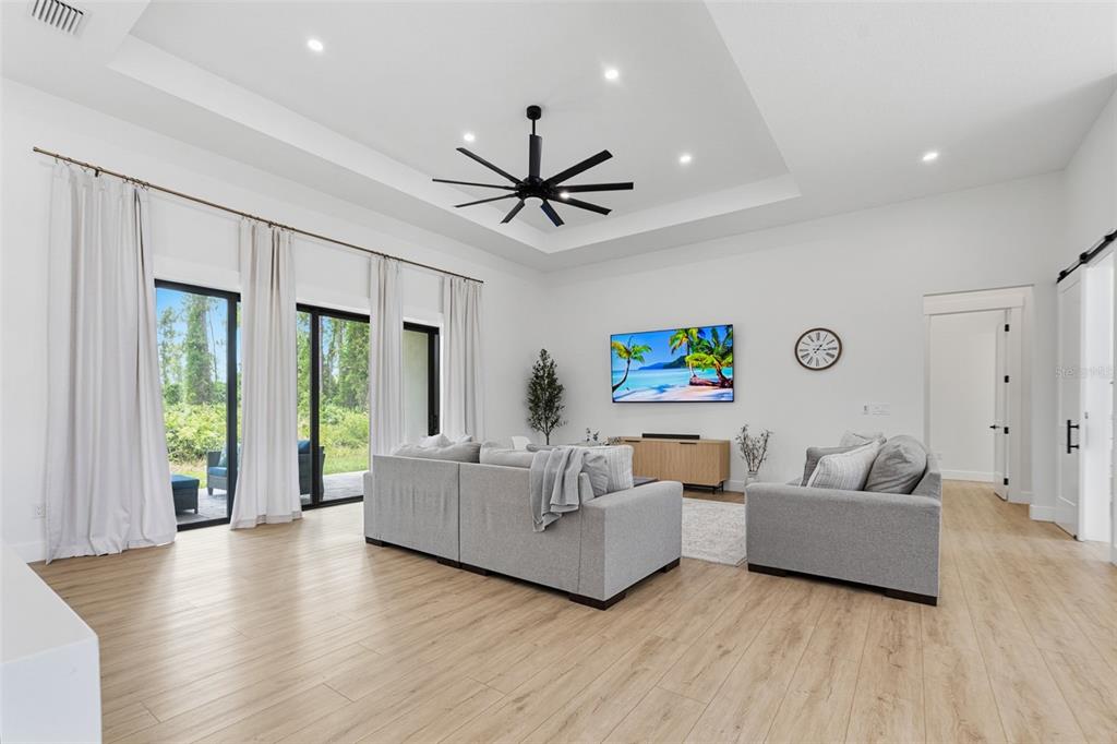 A bright living room features light wood flooring, a tray ceiling, and a large sectional sofa — 2777 LUCAYA AVENUE, NORTH PORT, FL
