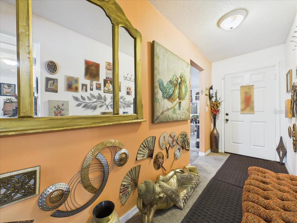 An entryway features orange walls, a large mirror, decorative fans, and a reclining Buddha statue — 3314 NW 45TH AVENUE, GAINESVILLE, FL