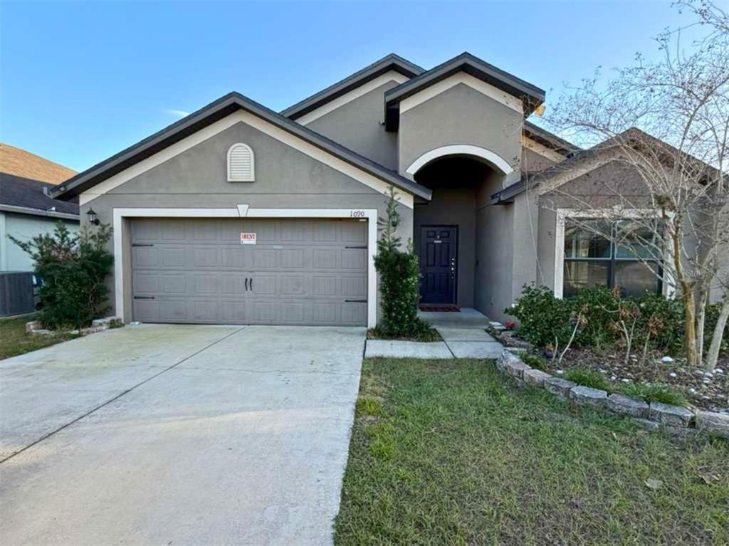 A single-story house with a gray stucco exterior, a two-car garage, and a covered entryway — 1090 WOODLARK DRIVE, HAINES CITY, FL
