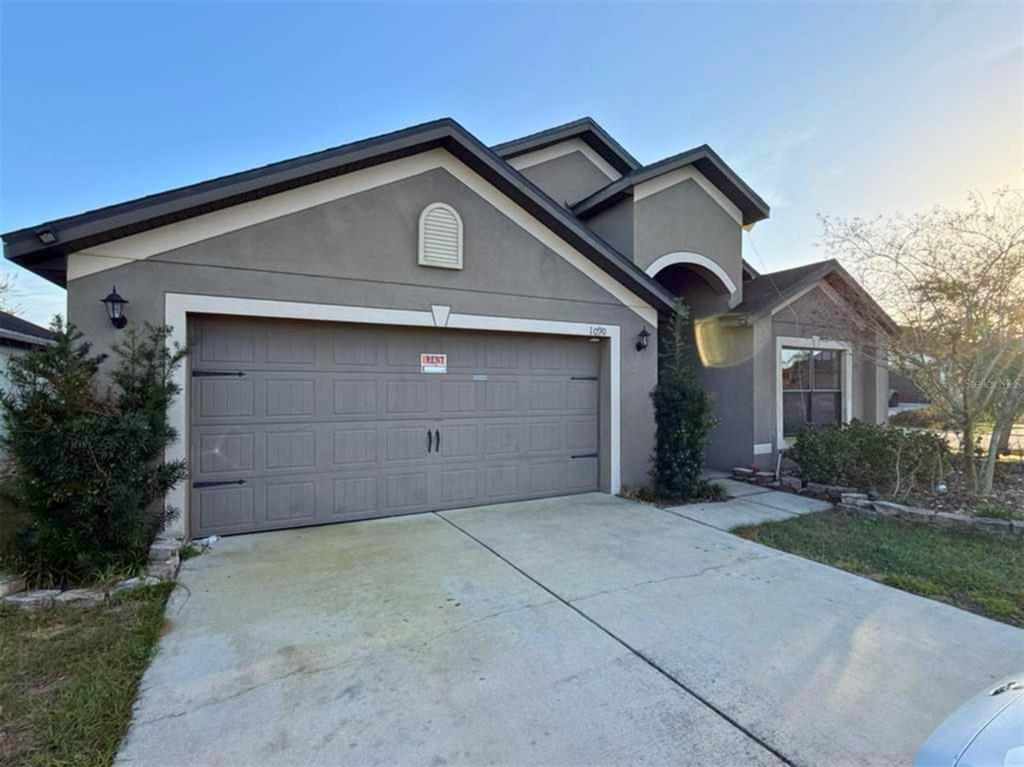 A single-story house with a gray stucco exterior, a two-car garage, and a concrete driveway — 1090 WOODLARK DRIVE, HAINES CITY, FL