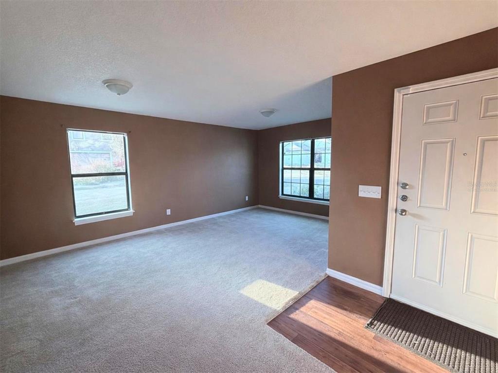 An empty living room features brown walls, beige carpeting, and a white front door — 1090 WOODLARK DRIVE, HAINES CITY, FL