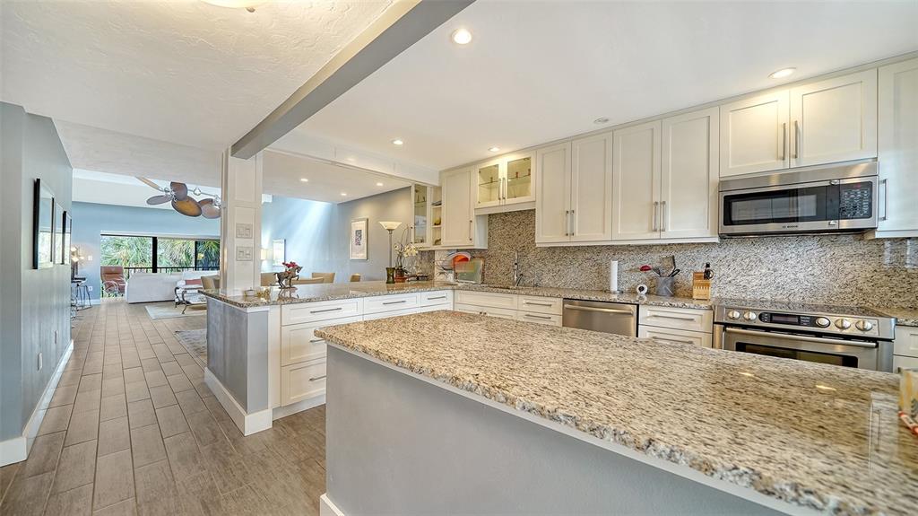 A kitchen with white cabinets, granite countertops, and stainless steel appliances overlooks a living area — 1601 PELICAN POINT DRIVE UNIT HA212, SARASOTA, FL