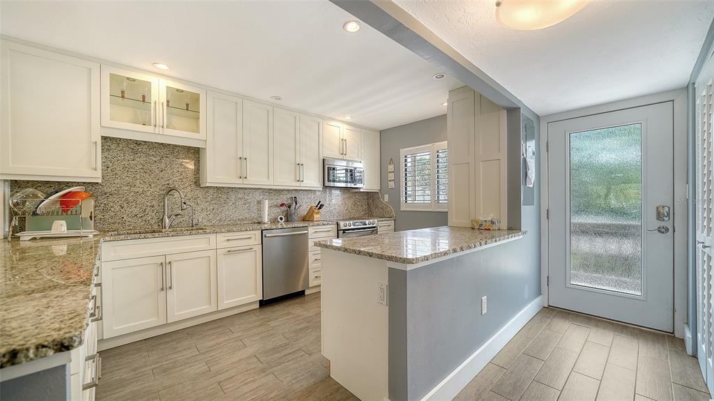 A kitchen with white cabinets, granite countertops, stainless steel appliances, and light wood-look tile flooring — 1601 PELICAN POINT DRIVE UNIT HA212, SARASOTA, FL