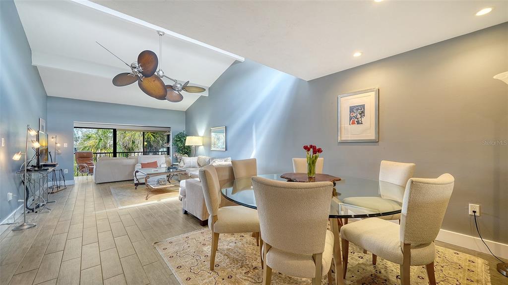 A dining area with a glass table and chairs opens into a living room space — 1601 PELICAN POINT DRIVE UNIT HA212, SARASOTA, FL