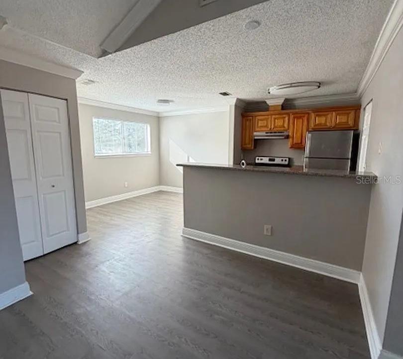 A kitchen with wood cabinets and stainless steel appliances overlooks a living area with flooring — 7298 ULMERTON ROAD UNIT 605, LARGO, FL