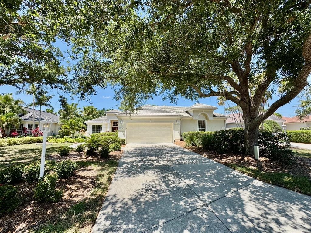 A single-story house with a beige exterior, a two-car garage, and a large shade tree — 7330 KENSINGTON COURT, BRADENTON, FL