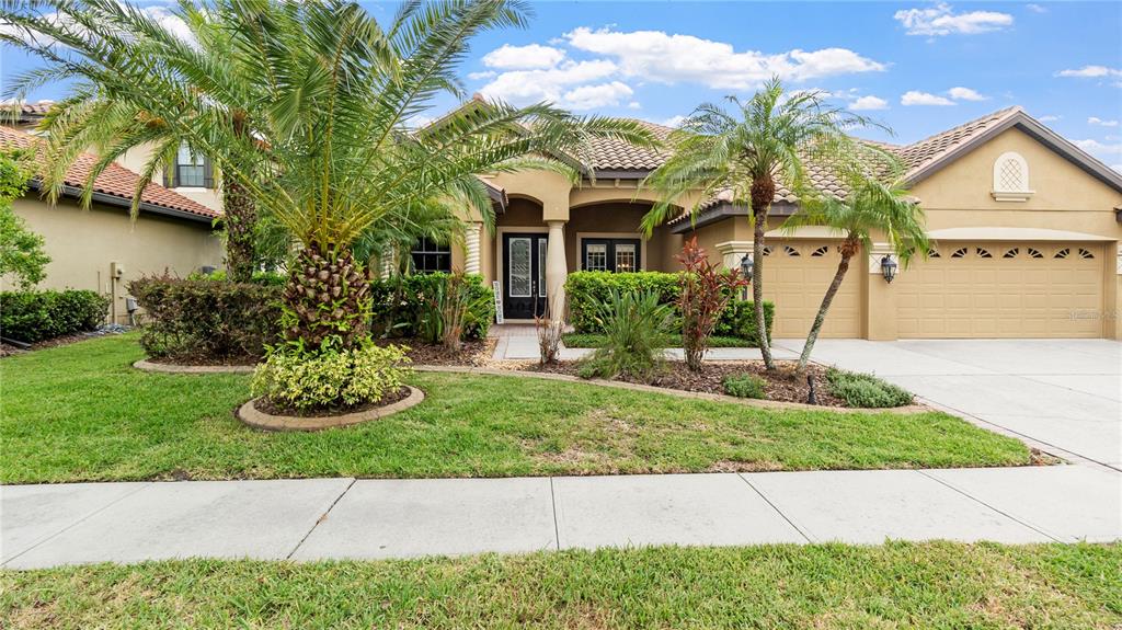 A single-story stucco house features a tile roof, a three-car garage, and palm trees — 20023 PERGOLA BEND LANE, TAMPA, FL