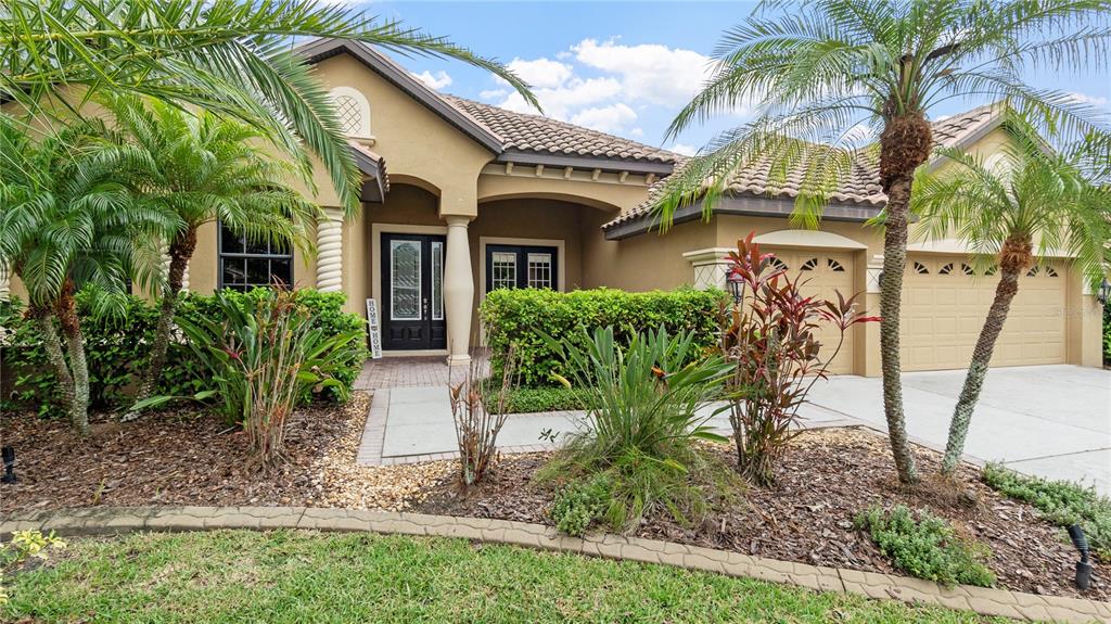 The exterior of a tan stucco house features a tiled roof, palm trees, and landscaping — 20023 PERGOLA BEND LANE, TAMPA, FL