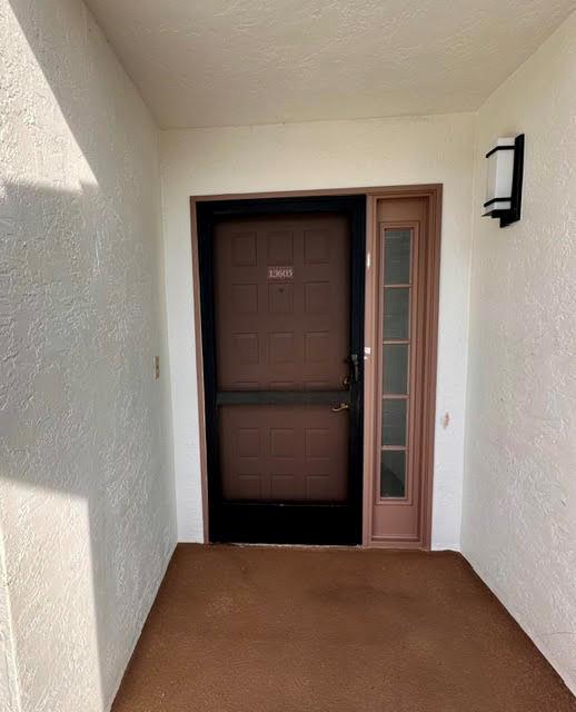 A brown front door with a black storm door and a side window under a porch — 7344 Clunie Place # 13605, Delray Beach FL 33446, DELRAY BEACH, FL
