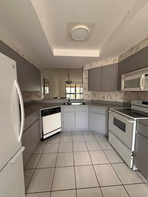 A kitchen features gray cabinets, white appliances, tiled flooring, and a pass-through window — 7344 Clunie Place # 13605, Delray Beach FL 33446, DELRAY BEACH, FL
