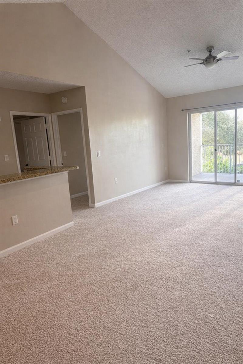 An empty living room with beige carpet, vaulted ceilings, a breakfast bar, and sliding glass doors — 272 Village Boulevard Unit 7305, Tequesta FL 33469, TEQUESTA, FL