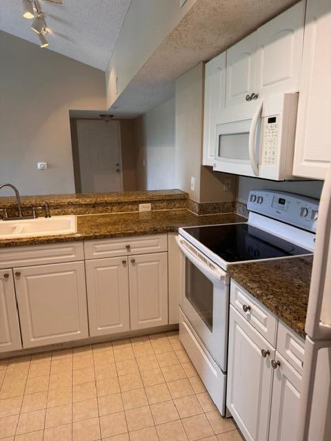 A kitchen features white cabinets, granite countertops, a white stove, and a microwave — 272 Village Boulevard Unit 7305, Tequesta FL 33469, TEQUESTA, FL