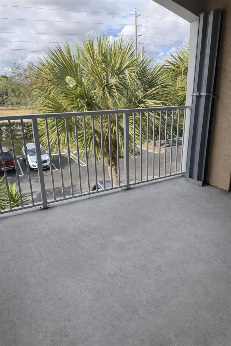 A concrete balcony features a white metal railing overlooking a parking lot and palm trees — 272 Village Boulevard Unit 7305, Tequesta FL 33469, TEQUESTA, FL