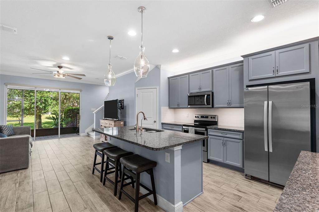 A kitchen with gray cabinets, granite countertops, and an island with bar stools — 14221 PONDHAWK LANE, TAMPA, FL