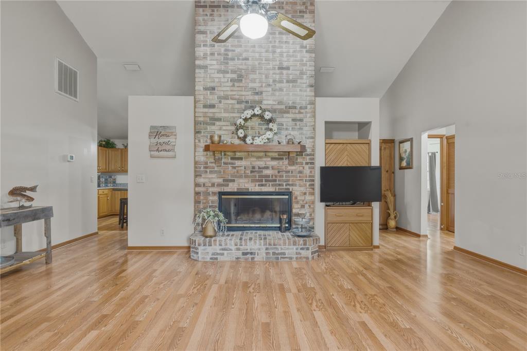 A living room features a tall brick fireplace, hardwood floors, and a vaulted ceiling — 26 COUNT FLEET DRIVE, OCALA, FL