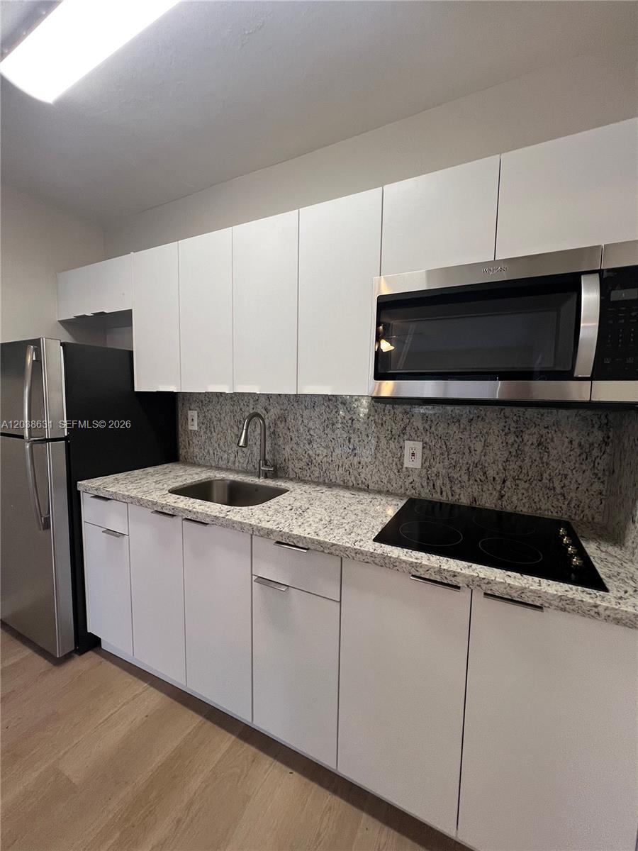 A kitchen features white cabinets, granite countertops, stainless steel appliances, and light wood flooring — 361 Sharar Ave # 6, Opa-Locka FL 33054, OPA-LOCKA, FL