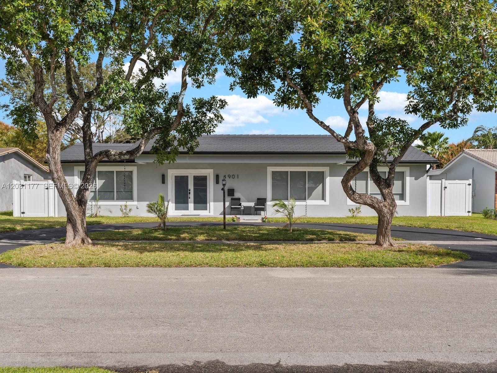 A single-story gray house with a dark roof sits behind two large trees — 4901 Grant St, Hollywood FL 33021, HOLLYWOOD, FL