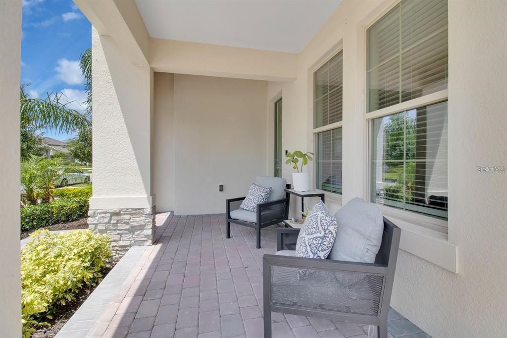 A covered front porch features paver flooring, stone accents, and two chairs with patterned pillows — 8768 SONOMA COAST DRIVE, WINTER GARDEN, FL