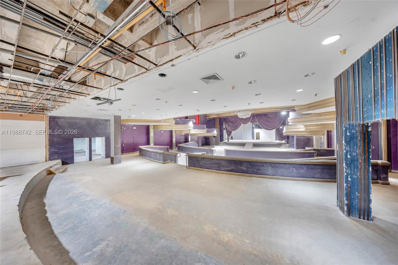 An unfinished, open-plan commercial space features tiered seating platforms, purple walls, and exposed ceiling infrastructure — 5445 Collins Ave, Miami Beach FL 33140, MIAMI BEACH, FL