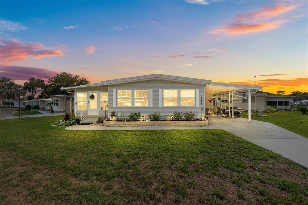A single-story manufactured home with light siding, a front porch, and an attached carport — 141 AZALEA TRAIL, LEESBURG, FL