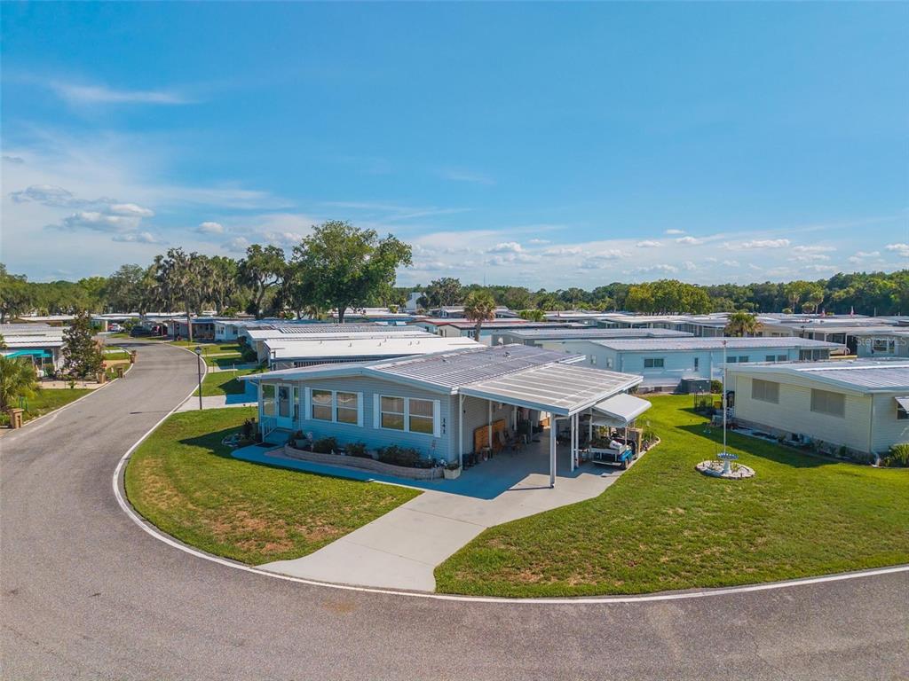 An exterior view of a light blue manufactured home with a carport in a community — 141 AZALEA TRAIL, LEESBURG, FL