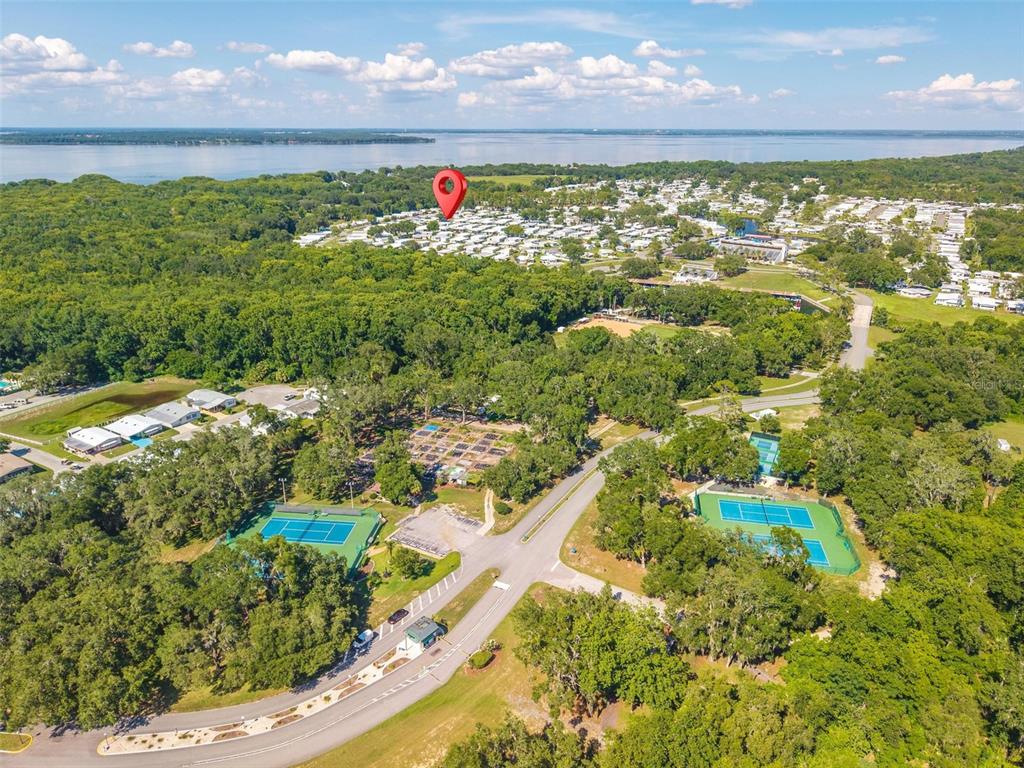 An aerial view shows a residential community with tennis courts, trees, and a distant lake — 141 AZALEA TRAIL, LEESBURG, FL
