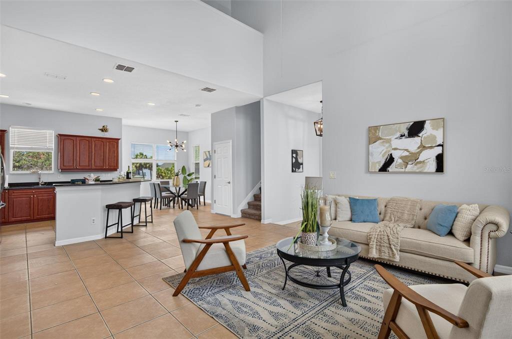 An open-concept living room and kitchen with tile floors, a beige sofa, and high ceilings — 7327 BRIGHTWATERS COURT, NEW PORT RICHEY, FL