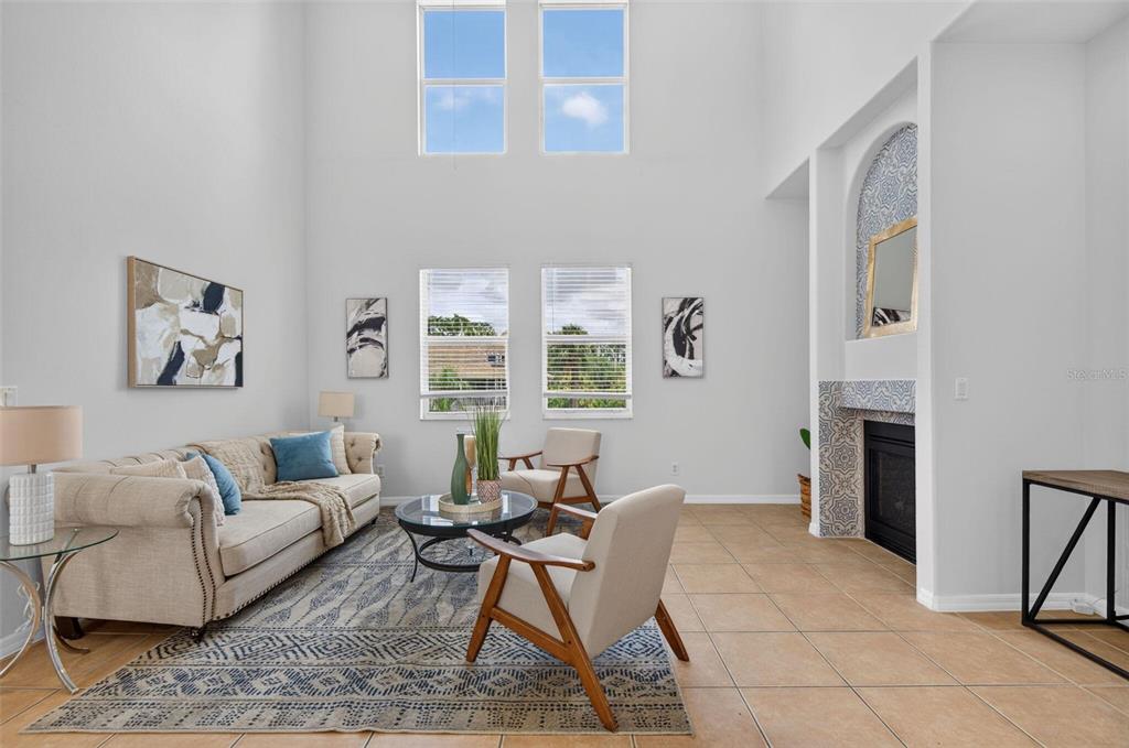 A living room features high ceilings, a tiled floor, a fireplace, and a large area rug — 7327 BRIGHTWATERS COURT, NEW PORT RICHEY, FL