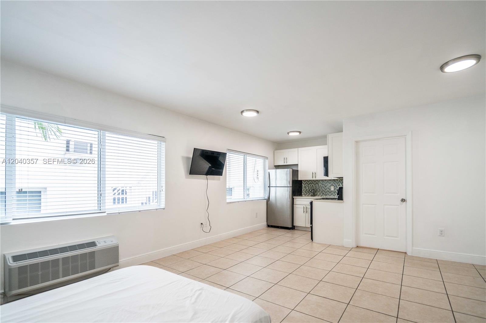 A studio apartment features a kitchenette, tiled floors, a wall-mounted television, and a window unit — 6971 Carlyle Ave # 107, Miami Beach FL 33141, MIAMI BEACH, FL