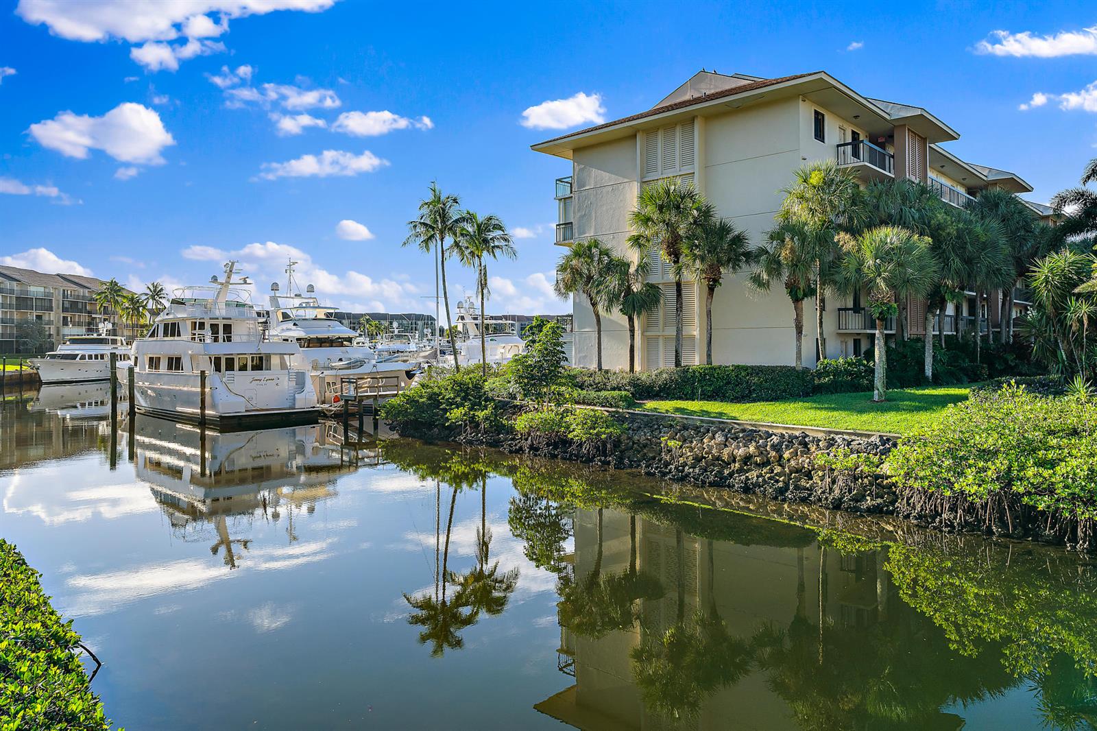 A multi-story apartment building sits beside a canal filled with docked yachts and palm trees — 2601 Marina Isle Way # 402, Jupiter FL 33477, JUPITER, FL