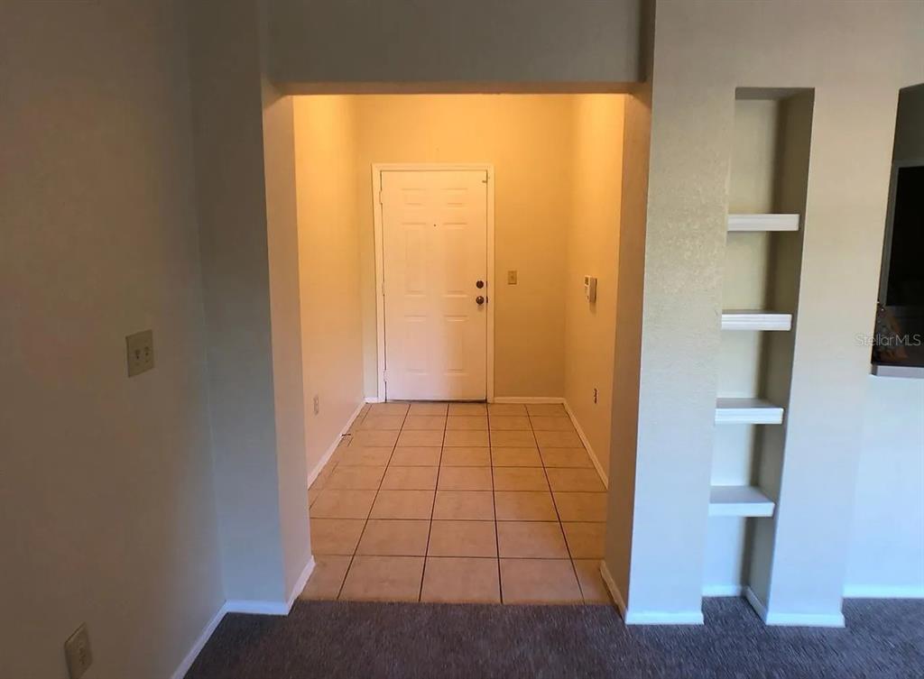 A tiled entryway leads to a white front door with built-in wall shelving nearby — 132 VISTA VERDI CIRCLE UNIT 228, LAKE MARY, FL