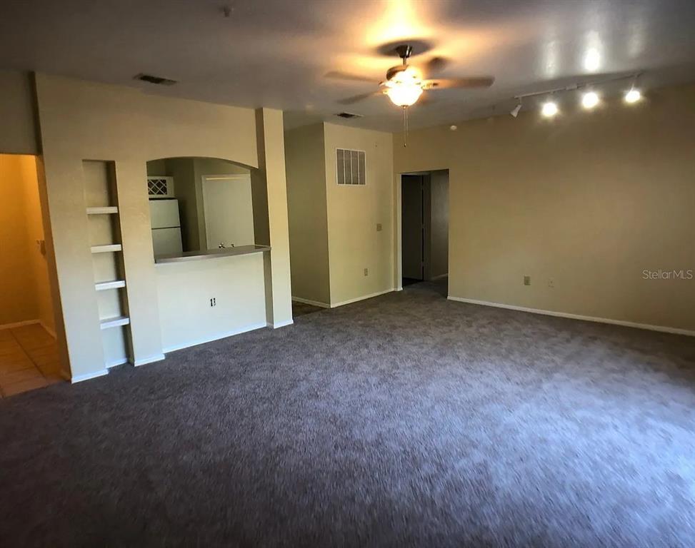 A spacious living room features gray carpeting, a ceiling fan, and a built-in shelving unit — 132 VISTA VERDI CIRCLE UNIT 228, LAKE MARY, FL