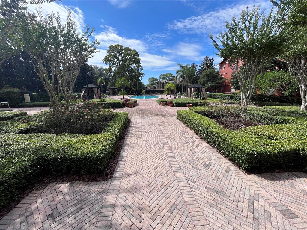 A brick walkway leads through a landscaped courtyard toward a swimming pool and cabanas — 132 VISTA VERDI CIRCLE UNIT 228, LAKE MARY, FL