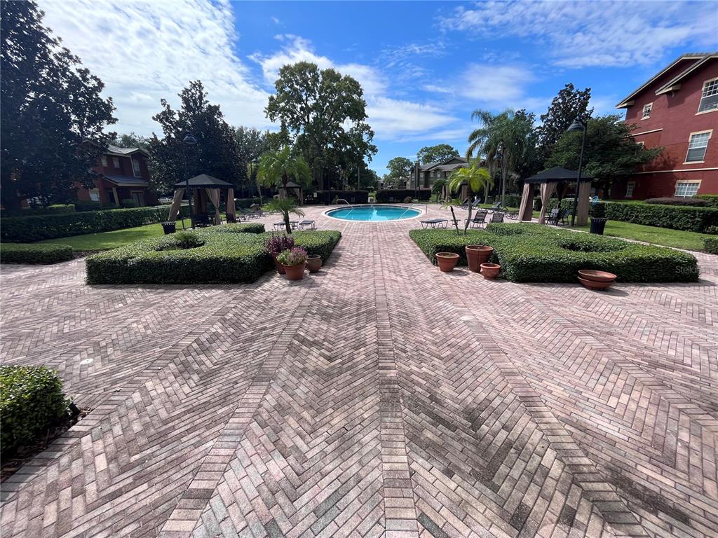 A brick-paved courtyard features a swimming pool, manicured hedges, and covered seating areas — 132 VISTA VERDI CIRCLE UNIT 228, LAKE MARY, FL