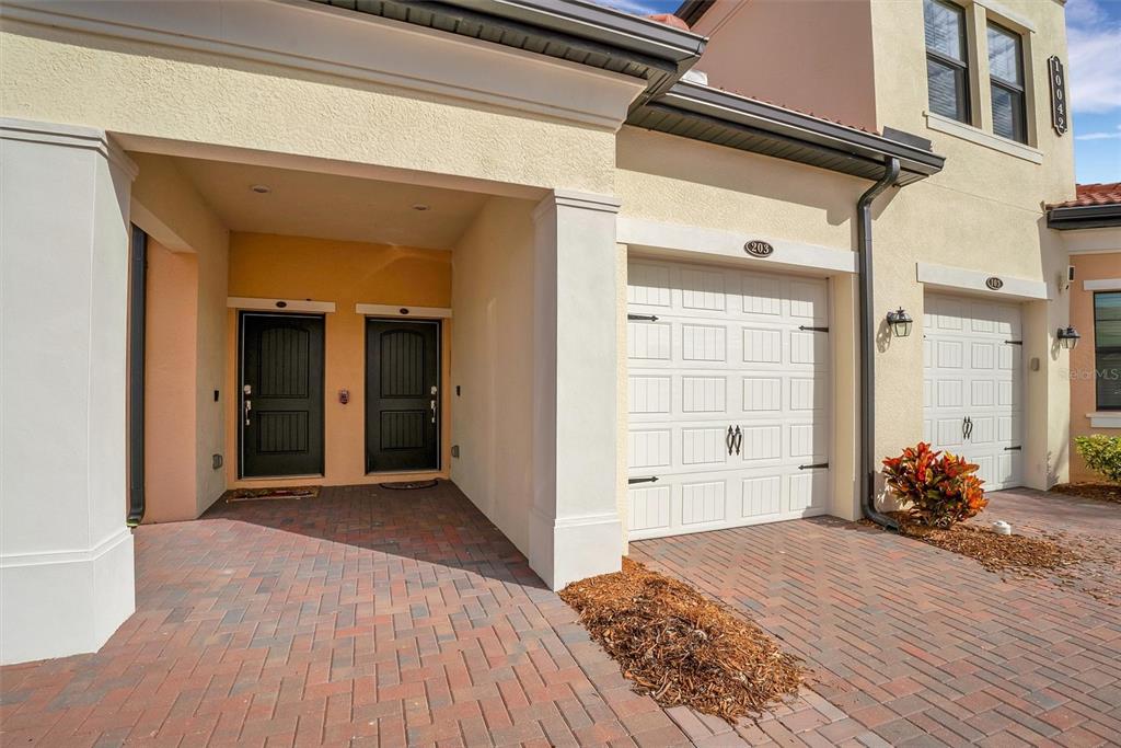 An exterior view of a residential building featuring two dark front doors and two garages — 10042 CROOKED CREEK DRIVE UNIT 203, VENICE, FL