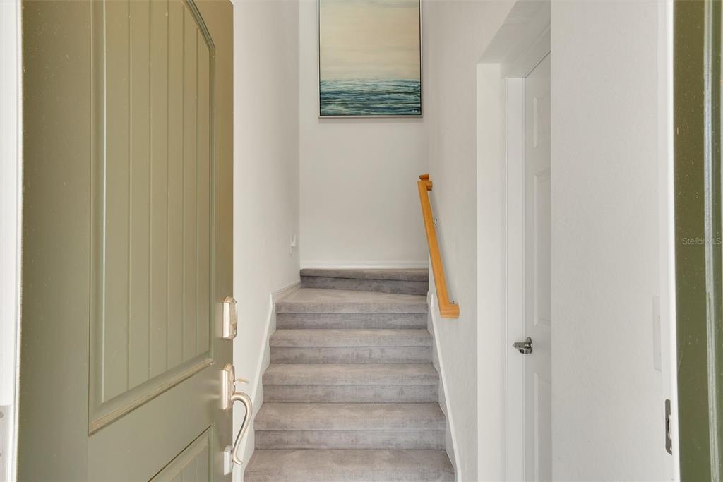 A carpeted staircase leads upward from an entryway with a green door and white walls — 10042 CROOKED CREEK DRIVE UNIT 203, VENICE, FL