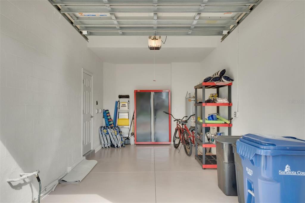A clean, one-car garage with white walls, a concrete floor, and various storage items — 10042 CROOKED CREEK DRIVE UNIT 203, VENICE, FL