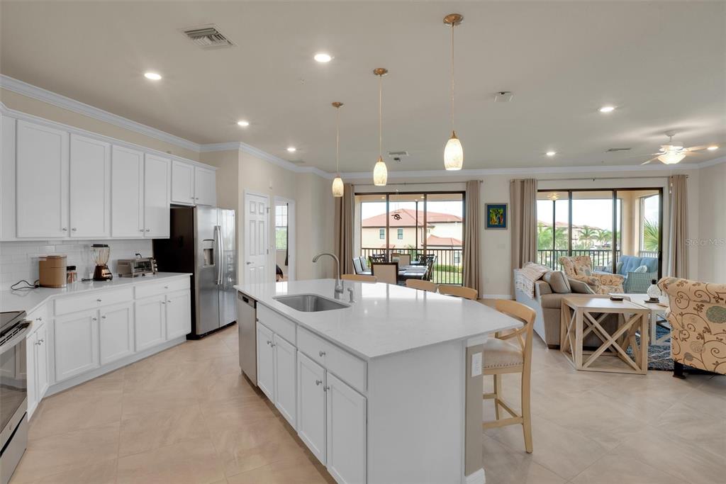 A white kitchen with a large island and stainless steel appliances opens to a living area — 10042 CROOKED CREEK DRIVE UNIT 203, VENICE, FL