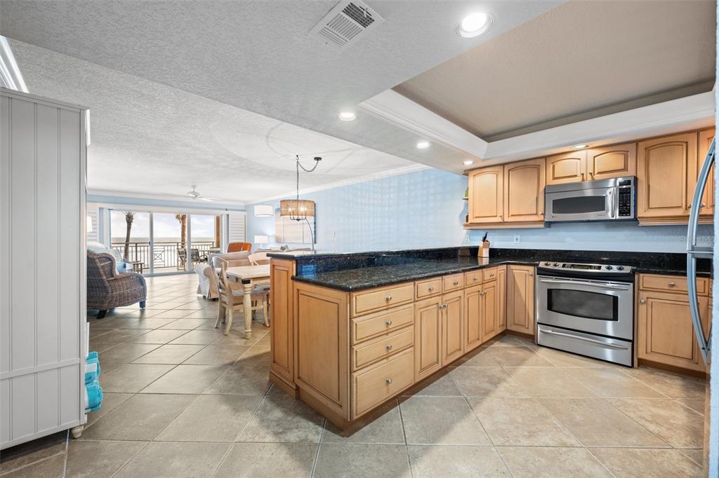 A kitchen with light wood cabinets and dark granite countertops opens to a living area — 5501 S ATLANTIC AVENUE UNIT 306, NEW SMYRNA BEACH, FL