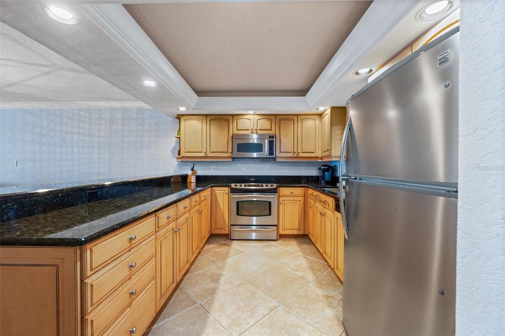A kitchen features light wood cabinets, dark granite countertops, stainless steel appliances, and tile flooring — 5501 S ATLANTIC AVENUE UNIT 306, NEW SMYRNA BEACH, FL