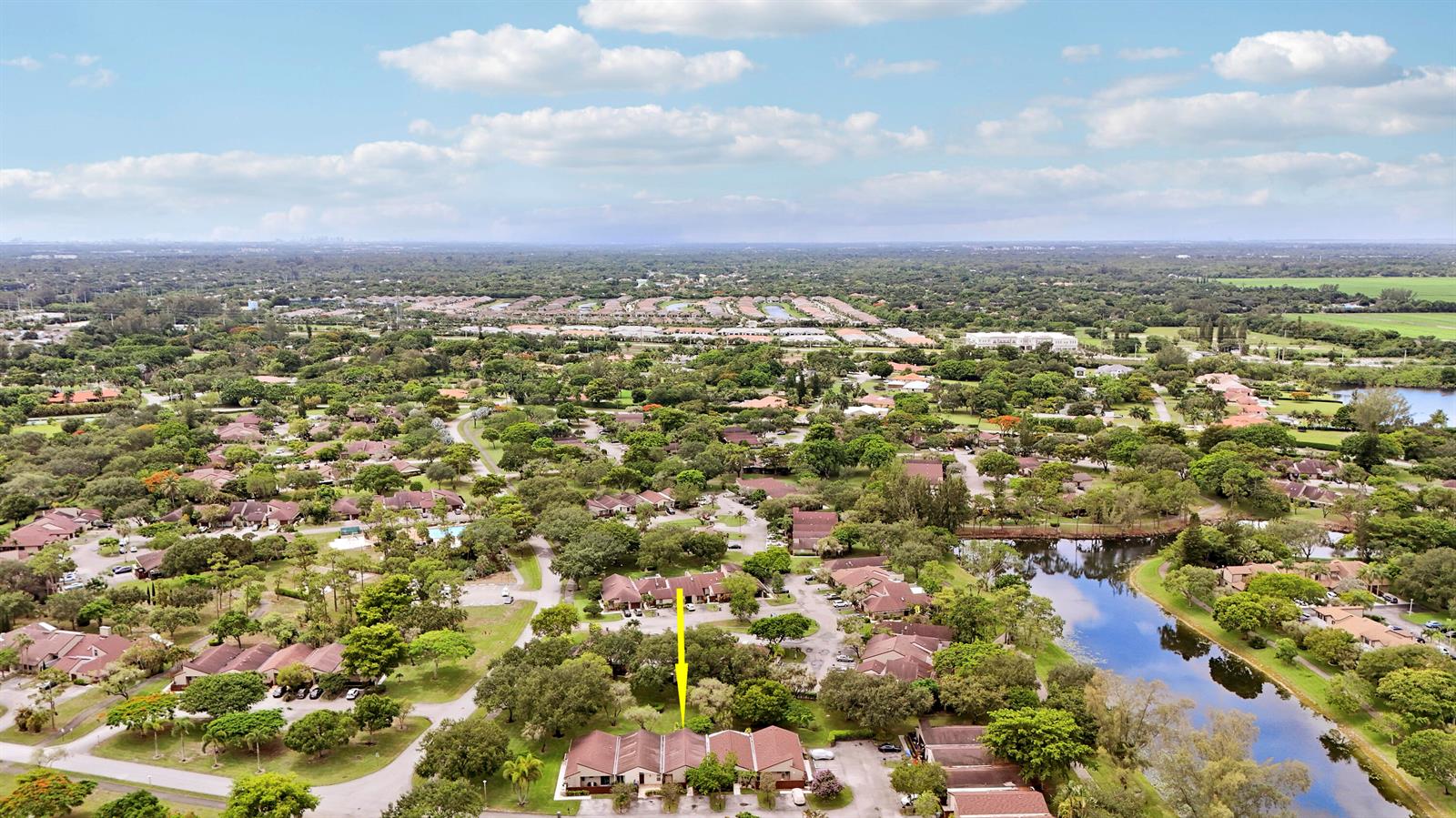 An aerial view shows a residential townhouse complex surrounded by trees and a nearby lake — 11606 Orange Blossom Lane, Boca Raton FL 33428, BOCA RATON, FL
