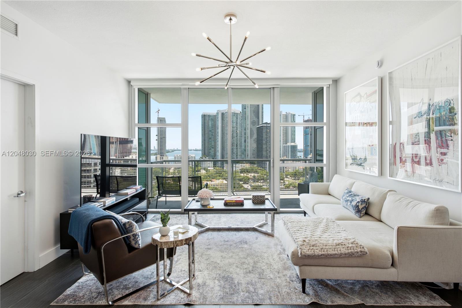 A modern living room features a white sectional sofa, leather armchair, and floor-to-ceiling city views — 3301 NE 1st Ave # H1704, Miami FL 33137, MIAMI, FL