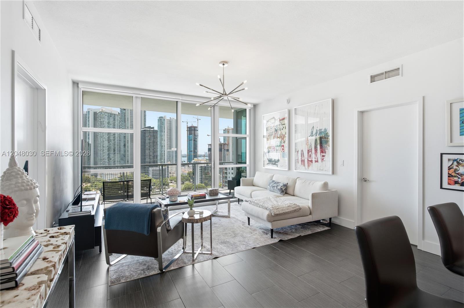 A modern living room features a white sectional sofa, dark flooring, and floor-to-ceiling city views — 3301 NE 1st Ave # H1704, Miami FL 33137, MIAMI, FL