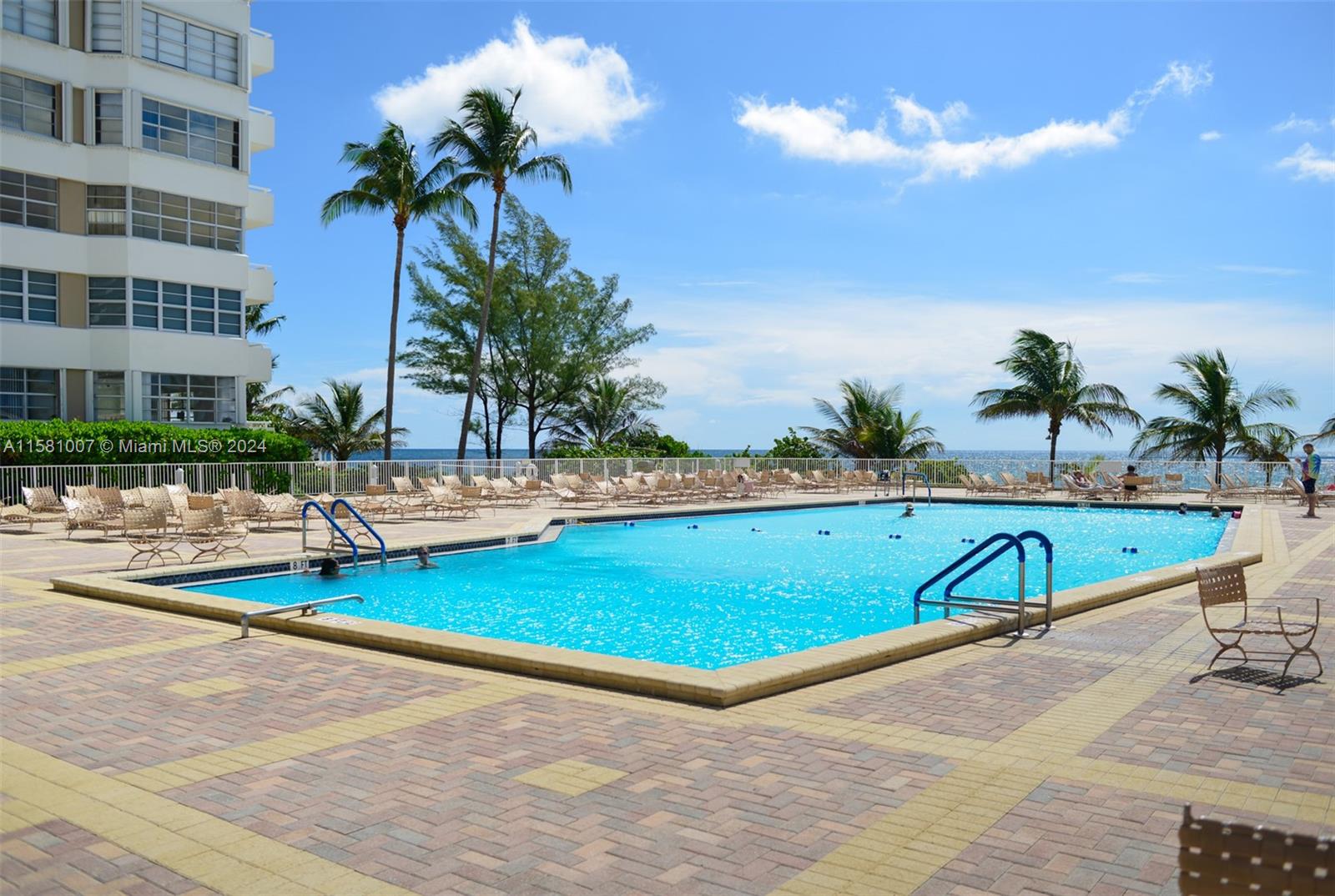 A large rectangular swimming pool sits on a paved deck beside a multi-story residential building — 1950 S Ocean Dr # 21G, Hallandale Beach FL 33009, HALLANDALE BEACH, FL