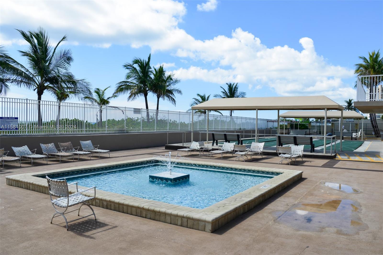 A square fountain sits on a pool deck with lounge chairs and a shaded area — 1950 S Ocean Dr # 21G, Hallandale Beach FL 33009, HALLANDALE BEACH, FL