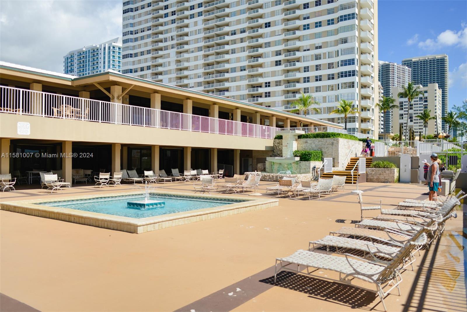 A pool deck features a small fountain, numerous lounge chairs, and a multi-story residential building — 1950 S Ocean Dr # 21G, Hallandale Beach FL 33009, HALLANDALE BEACH, FL