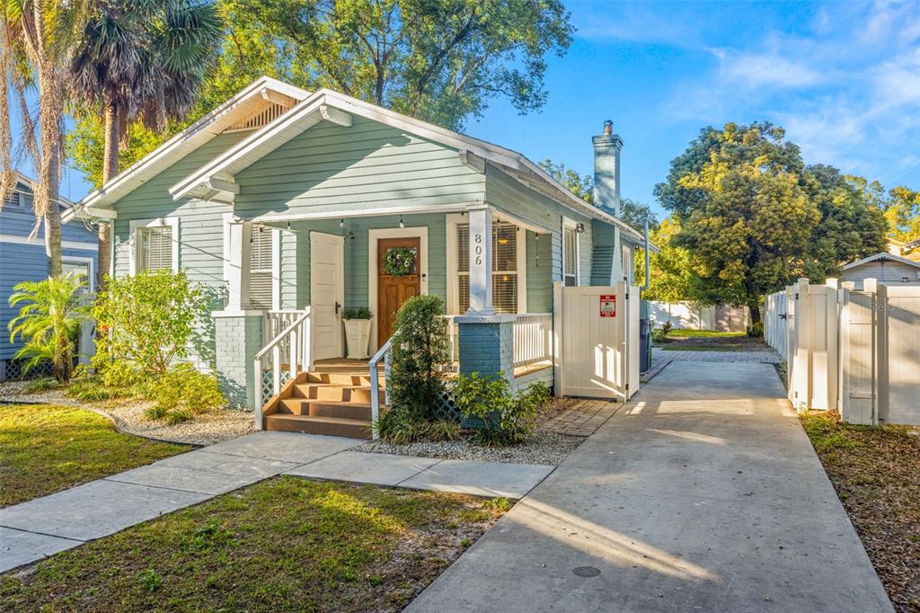 A light blue bungalow with a front porch, concrete driveway, and white vinyl fencing — 806 E GENESEE STREET, TAMPA, FL