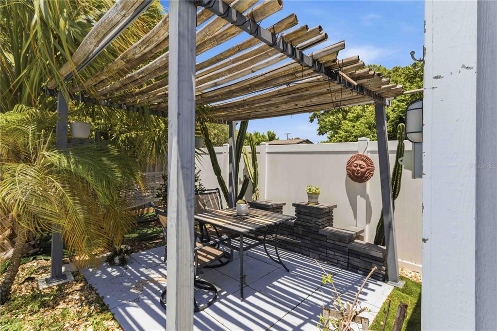 A patio features a bamboo-slatted pergola, a metal dining set, and a decorative sun wall hanging — 2713 W BRADDOCK STREET, TAMPA, FL